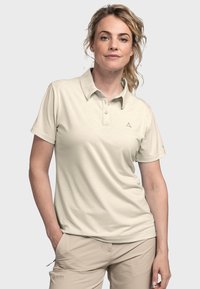 Beige Poloshirt mit Kragen, drei Knöpfen und einem dezenten Logo auf der Brust. Glatter Stoff und kurze Ärmel kombiniert mit hellbraunen Stoffhosen.