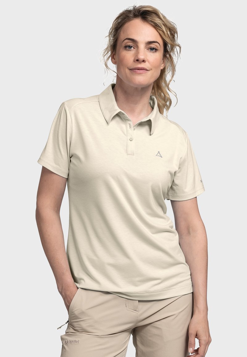 Beige Poloshirt mit Kragen, drei Knöpfen und einem dezenten Logo auf der Brust. Glatter Stoff und kurze Ärmel kombiniert mit hellbraunen Stoffhosen.