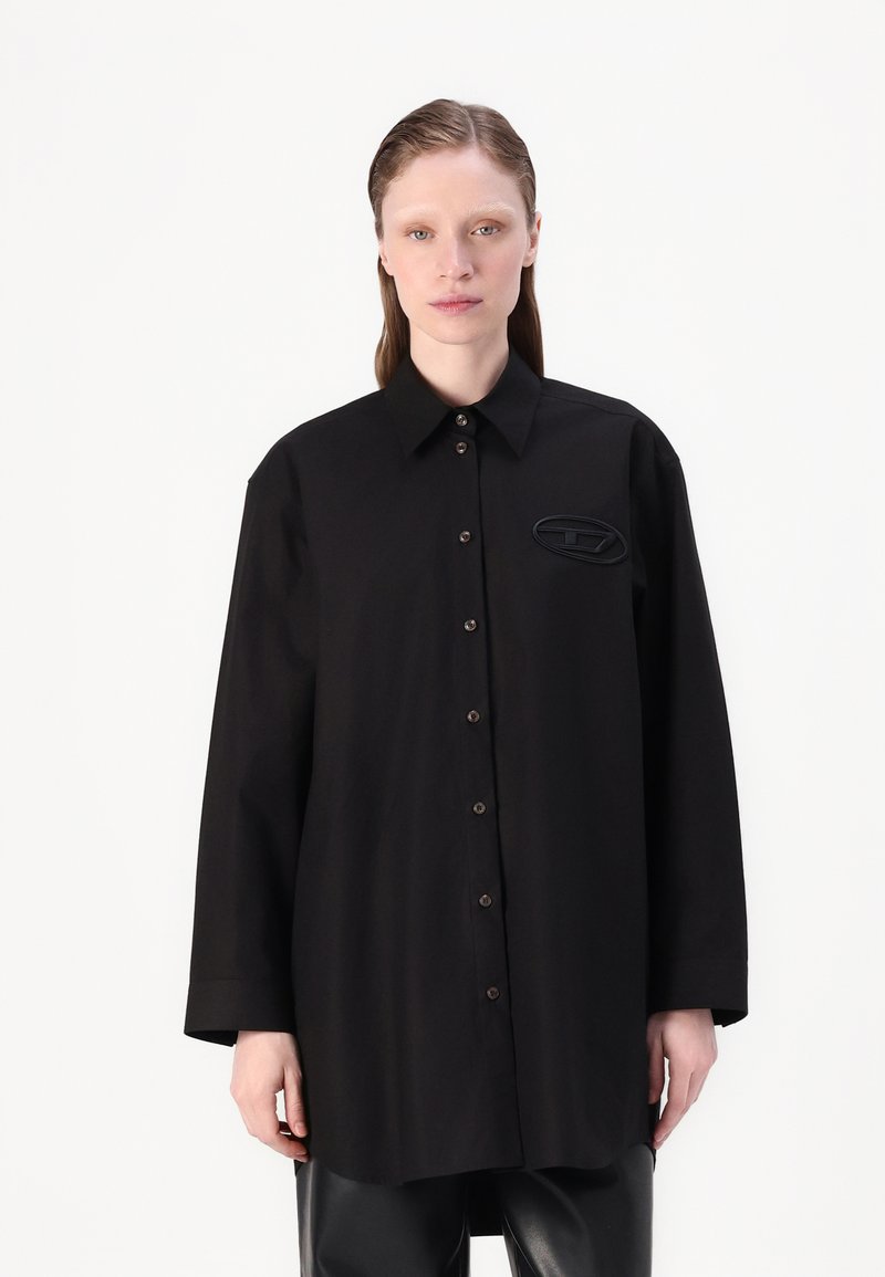Black long-sleeve shirt with a collar, button front, and an oval logo on the left chest. Made of smooth fabric with a relaxed fit.