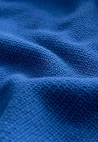 Tissu tricoté à texture douce de couleur bleu vif avec des motifs de points visibles et des plis délicats.
