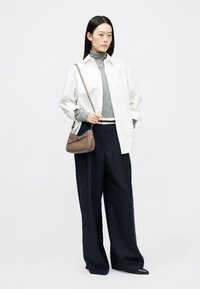 Balta pārmērīga krekla, pelēka augsta apkakles blūze, tumši zilas svītrainas platās bikses un brūna ādas plecu soma ar viegli izliekta dizaina.