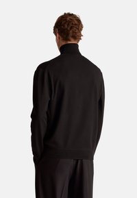 Schwarzer, hochgeschlossener Pullover mit glatter Textur, langen Ärmeln und gerippten Bündchen. Entworfen mit einem lässigen Schnitt und minimalen Akzenten.