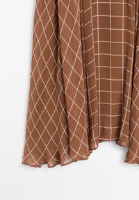 Braun gemusterter Stoff mit einem Karodesign und cremefarbenen Linien, der sanft hängt. Die Textur wirkt leicht und durchsichtig, mit einer fließenden Silhouette.