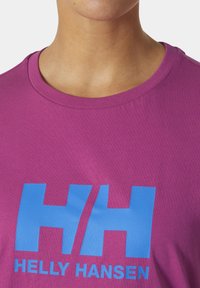 Camiseta de algodón morada con un gran logotipo azul "HH" y el texto "HELLY HANSEN". Diseño de cuello redondo, textura suave y mangas cortas.