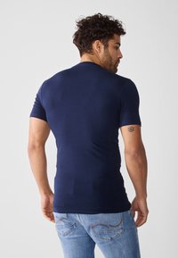 Marineblå kortermet t-skjorte med en tettsittende design; glatt tekstur. Brukt sammen med lyseblå jeans med subtile sømdetaljer.