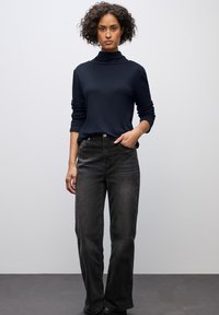 Marinefarbener Rollkragenpullover mit langen Ärmeln, kombiniert mit schwarzen geraden Jeans, die ein klassisches Design und eine dezente, ausgewaschene Textur aufweisen.
