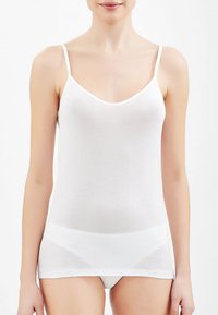 Camisola bianca con spalline sottili, realizzata in un tessuto leggero e testurizzato. Presenta un scollo a barca e un design aderente.