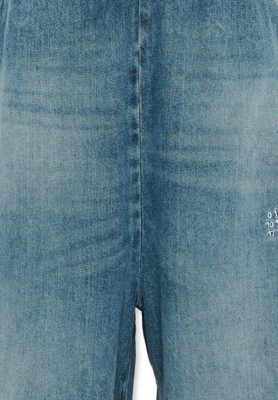 Gros plan sur un jean en denim bleu montrant la couture centrale et de petits chiffres blancs imprimés sur la zone de la cuisse droite.