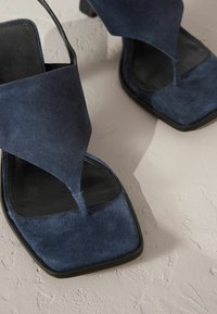 Åben tå højhælede sandaler lavet af marineblåt ruskind med en firkantet form og en blank sort indersål. Har et crossover-stroppedesign.