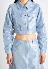 Ljusblå paljettkort jacka med guldknappar, två bröstfickor och långa ärmar, i kombination med en matchande paljettkjol med hög midja.