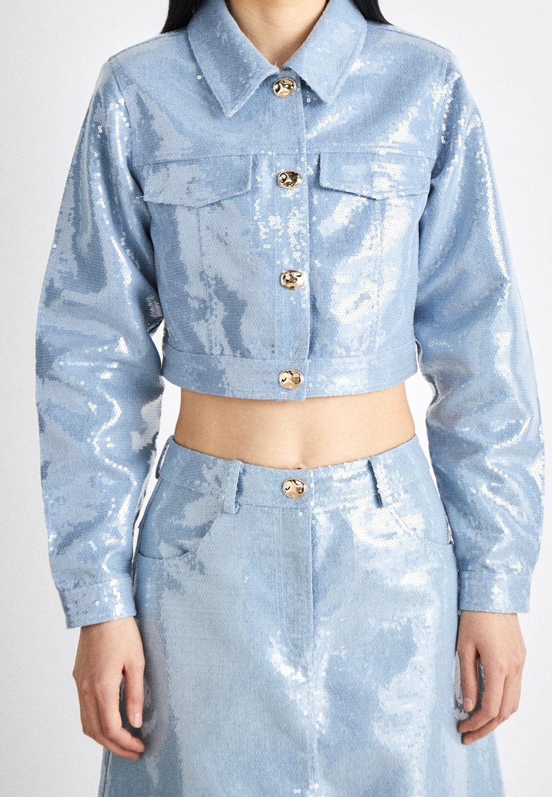 Ljusblå paljettkort jacka med guldknappar, två bröstfickor och långa ärmar, i kombination med en matchande paljettkjol med hög midja.