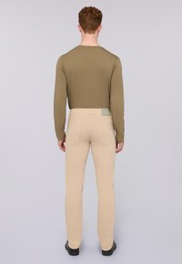 Top de manga larga verde oliva combinado con pantalones beige, que cuentan con una etiqueta en la parte trasera. Los pantalones tienen dos bolsillos traseros y un diseño ajustado.