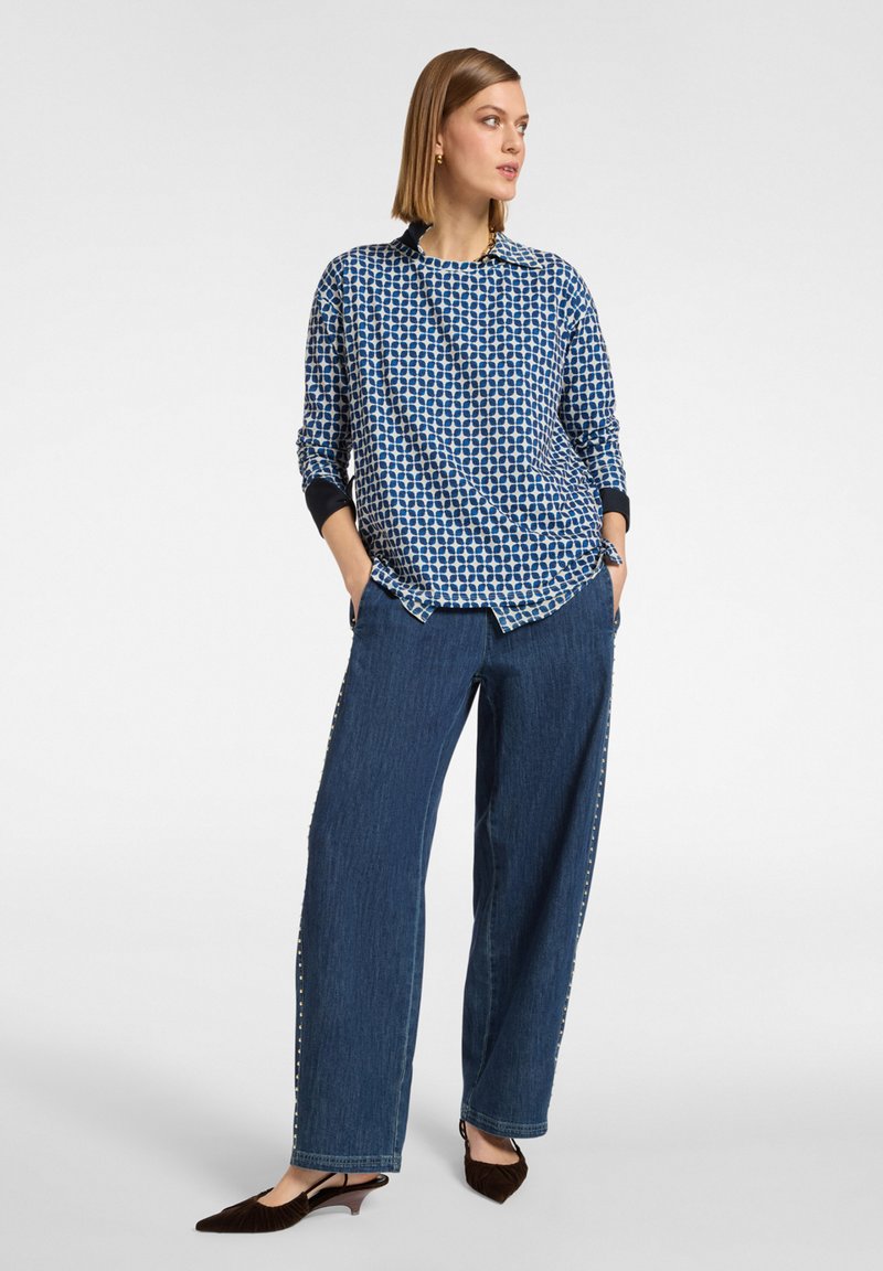 Blauw gemêleerd langärmelig shirt met een ronde halslijn, gecombineerd met wijde donkerdenim broek met zijstuds en bruine hakken.