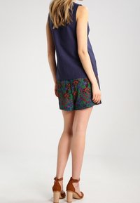 Haut sans manches bleu marine avec un col rond, associé à un short vert à motifs floraux. Sandales à talons marron complètent le look.