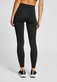 Zwarte leggings met hoge taille, voorzien van een aansluitend ontwerp, gladde textuur en versterkte naden, gecombineerd met zwarte sportschoenen.