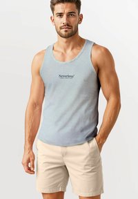 Light blue tank top with "Neverless Sunday Tennis Club" printed in dark text, combined with beige shorts, displayed on a male model.