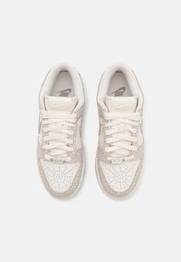 Nike sportcipők bézs bőr felsőrészsel, világos színű hálós nyelvvel és leopárdmintás díszítésekkel az oldalán. Klasszikus fűzős kialakítással rendelkezik.