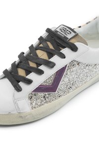 Sneaker bianca in pelle con accenti di glitter argento, lacci grigio scuro e un dettaglio in pelle viola. Suola in suede beige testurizzato nella parte superiore.