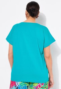 Top turquesa de manga corta con un ajuste holgado y escote redondo, combinado con leggings de estampado floral colorido. Textura de tela suave.