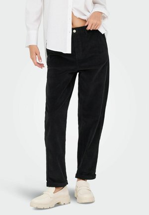 Sorte kordfløjspants med afslappet pasform, der har knaplukning, sidelommer og opkrøllede kanter, parret med hvide slip-on sko.
