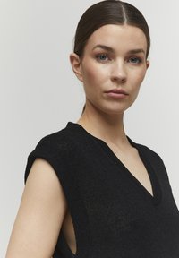 Top nero lavorato a maglia con scollatura a V, maniche corte e tessuto texturizzato, progettato con lati aperti per una vestibilità rilassata.