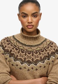 Pull en maille marron avec un col côtelé haut, présentant des motifs géométriques en marron foncé, vert et crème, avec une finition texturée.