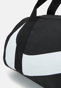 Black duffle bag with white curved stripe, made of durable fabric. Features sturdy black handles for easy carry.