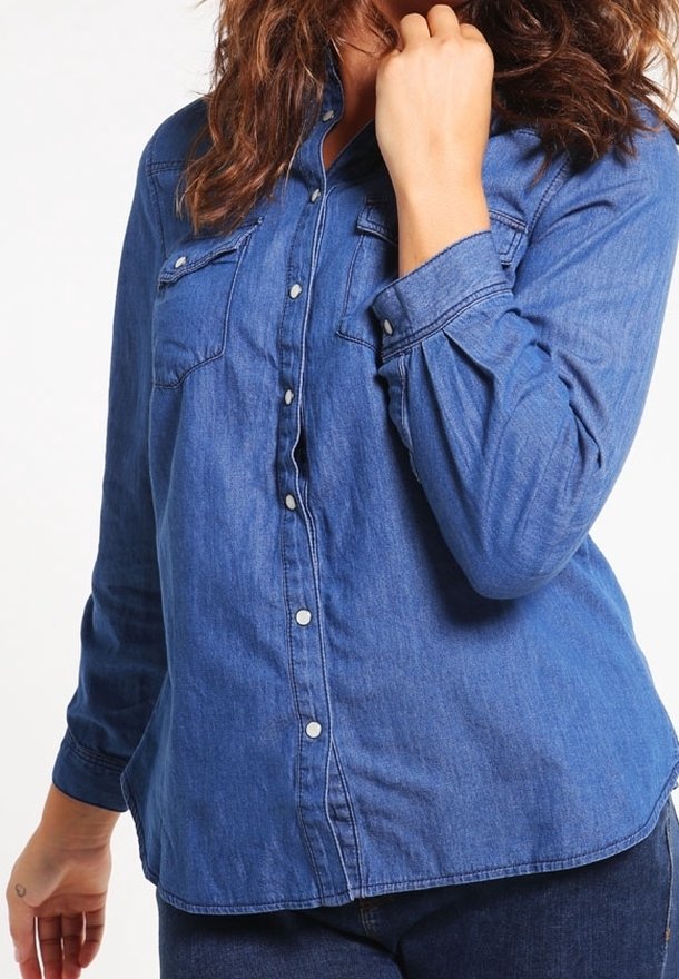 Denimskjorta med knappar i mörkblått, med två bröstfickor, långa ärmar och rundad nederkant med synlig knäppning.