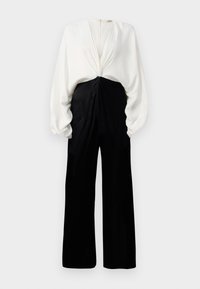 Mustvalge jumpsuit, millel on keeratud, volditud valge ülaosa ja laiad mustad püksid. Omab seljaosas üles tõmmatavat lukku ja volüümikad varrukad.