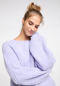 Világos lila kötött pulóver vastag bordás textúrával, ejtett vállakkal és oversized ujjak. Puha, tömör anyag, amely a melegségért készült.