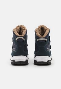 Par de botas de invierno Gore-Tex azul marino con forro de felpa beige, medias suelas blancas y suelas de goma negras vistas desde atrás.