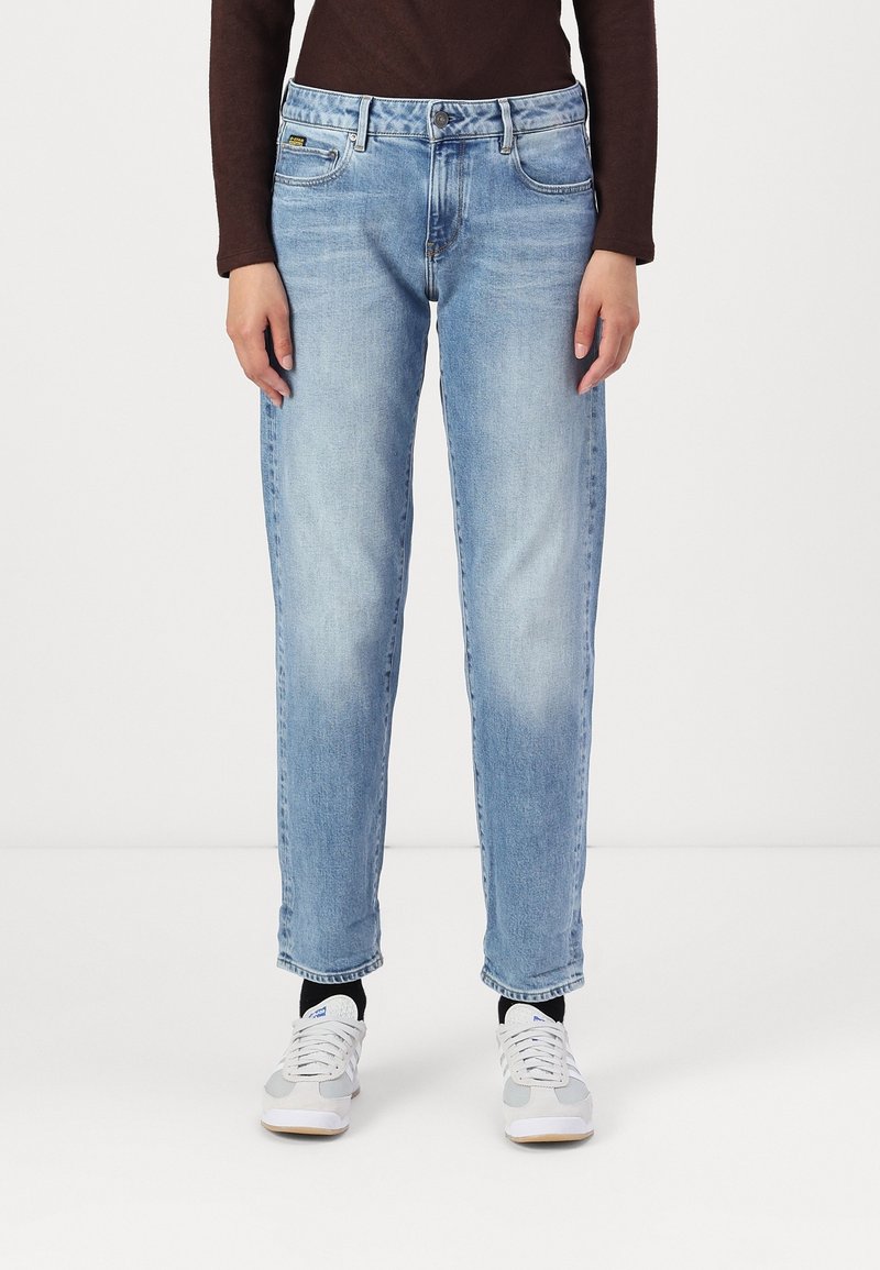 Light blue denim jeans with a straight fit, faded design, five-pocket style, and a button closure. Paired with gray and white sneakers.