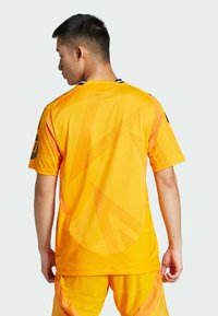 Maglia sportiva gialla con un motivo geometrico e maniche corte. Realizzata in materiale leggero con scollo rotondo e dettagli a contrasto.