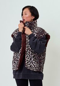 Pletená vesta so vzorom leopardích škvŕn v odtieňoch hnedej a smotanovej, s vínovou golierom. Mäkká tkanina; voľný, oversized dizajn.