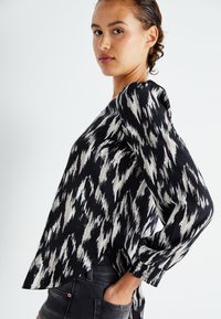 Zwart-wit geblokte blouse met lange mouwen, zachte stof, ronde zoom en elastische manchetten, met een ikatontwerp door het hele kledingstuk.