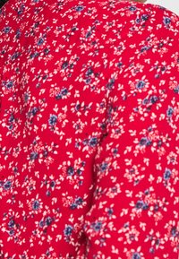 Roter Stoff mit einem floralen Muster, das kleine blaue und weiße Blumen zeigt, glatte Textur und leicht schimmernd. Geeignet für verschiedene Bekleidungsstücke.