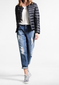 Černá péřová bunda s prošívaným designem, šedé tričko, opotřebované modré džíny a šedé tenisky. Ležérní outfit s uvolněným střihem.