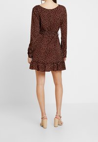 Musta, pitkähihaine mekko, jossa on valkoisia pilkkuja, röyhelöhelma ja vyötäröllä solmuseikka. Yhdistetty vaaleanvärisiin paksupohjaisiin sandaaleihin.