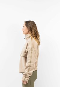 Beiger Fleece-Pullover mit hohem Kragen, Reißverschluss und Logo-Patch. Mit seitlichem Text, langen Ärmeln und lockerer Passform.