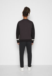 Svart och mörkgrå sweatshirt med vita randdetaljer på ärmarna, kombinerad med matchande mörka joggers och vita sneakers; slät textur.