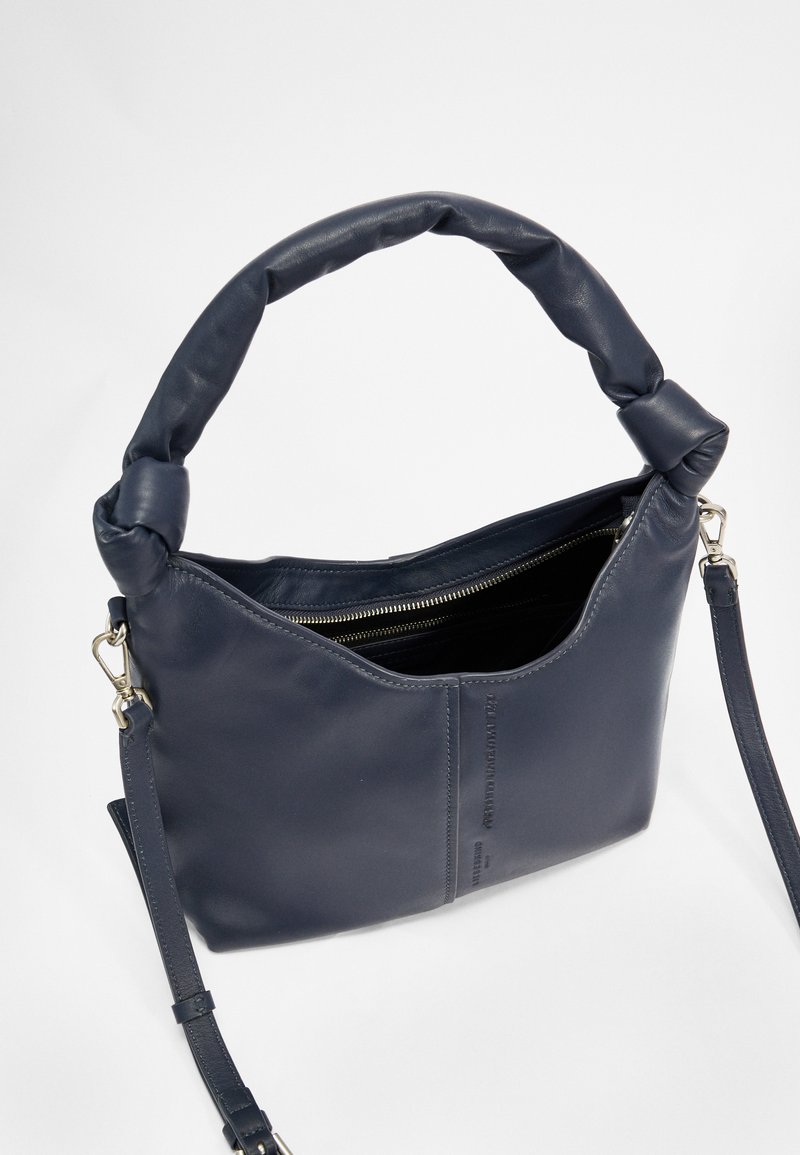 Marineblaues Lederhandtasche mit gedrehter Handhabung, Reißverschluss, weicher Textur und verstellbarem Schulterriemen. Das Innere scheint schwarz zu sein.