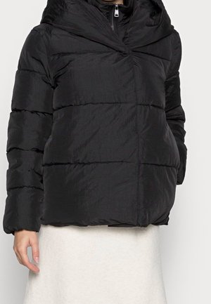 Czarna pikowana kurtka puchowa z poziomym przeszyciem, wysokim kołnierzem, przednim suwakiem i bocznymi kieszeniami, noszona na jasnej spódnicy.