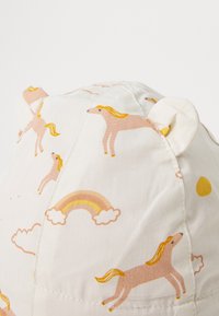 Gorra de algodón para niños con una base blanca y estampados de unicornios y arcoíris en tonos pastel. Incluye orejas de oso redondeadas en la parte superior para un detalle adicional.
