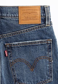 Blå denimjeans bakficka med orange sömnad, röd Levi's etikett och brun läderetikett från Levi Strauss & Co. ovanför fickan.