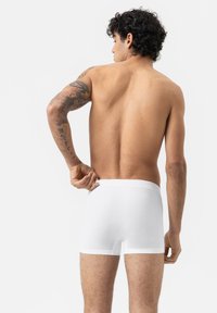 Boxers en coton blancs portés par une personne, mettant en valeur une texture lisse et un design ajusté, vus de derrière sur un fond uni.