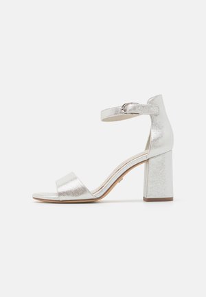Ezüst színű, magas sarkú szandál, amely blokk sarokkal, nyitott orral, bokapánttal és fém csattal rendelkezik, valamint fényes textúrával van ellátva.