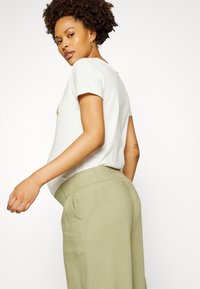 T-shirt branca de algodão com mangas curtas e decote redondo, combinada com calças de linho verde claro com cintura elástica.