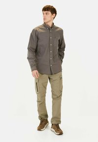 Grå skjorte med knapper og lomme, parret med beige cargo-bukser med sidelukninger og brune sneakers. Simpelt og klart design.