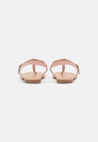 Sandales plates roses au design simple, avec une sangle texturée et une semelle en caoutchouc brun clair. Détail de boucle réglable au niveau de la cheville.