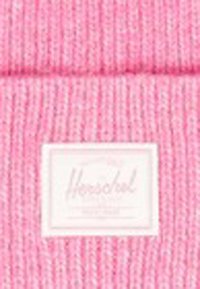 Gorro de punto rosa con textura acanalada. Presenta una etiqueta blanca rectangular de Herschel en la parte frontal. Distribución de color uniforme en todo el gorro.